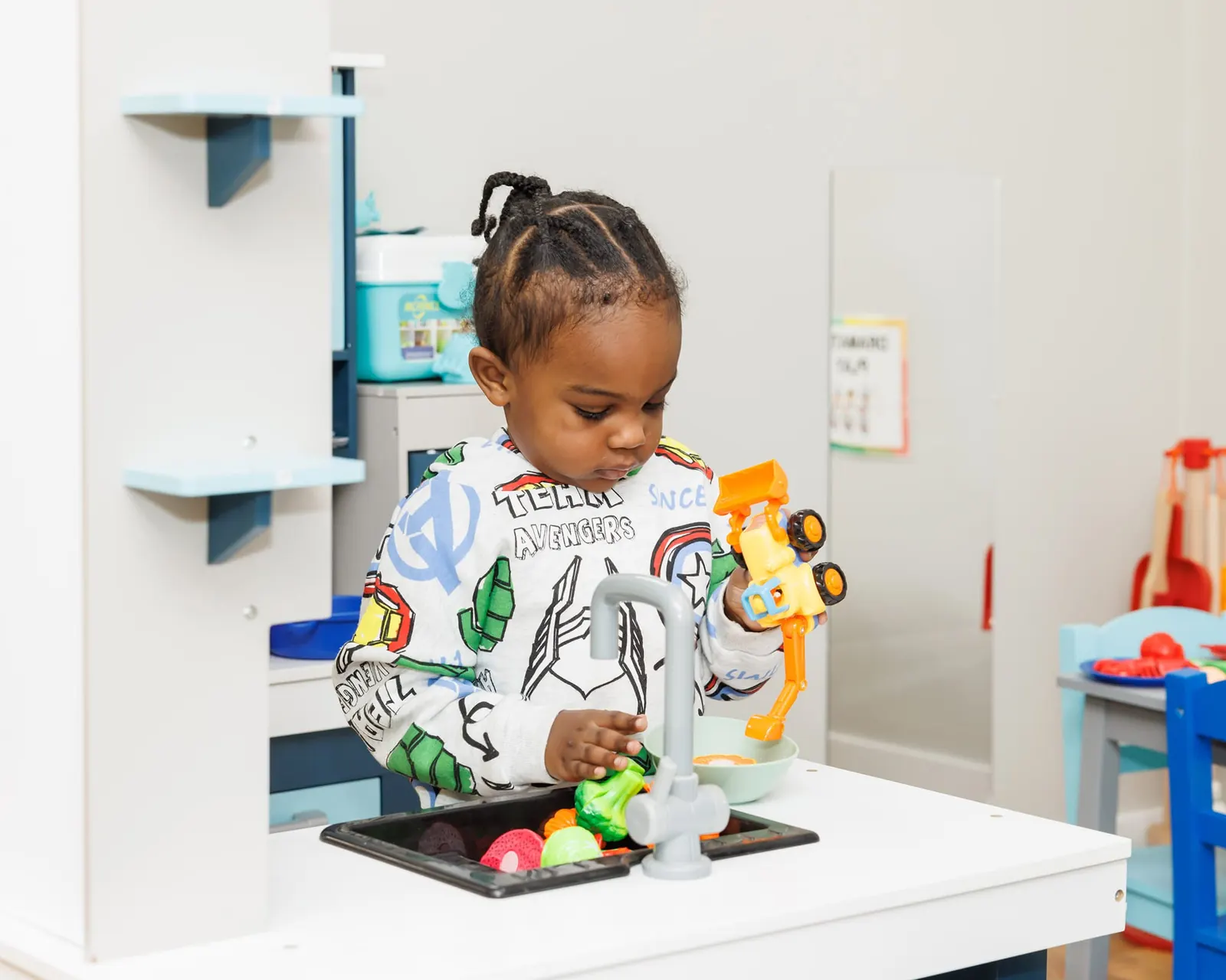 Toddler washing toy vegetables at a pretend play sink